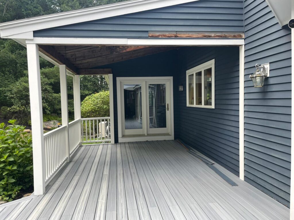 Completed blue composite deck in Westwood, MA by Monroy's Carpenters, Inc., featuring navy house siding, white railings, and French doors for outdoor access.