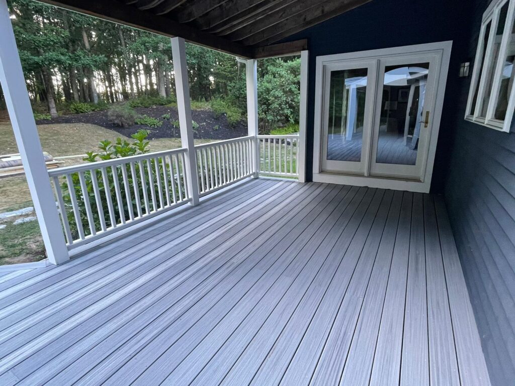 Angled shot of elevated deck steps and white balustrades against the blue house exterior in Westwood, MA, showcasing expert carpentry by Monroy's Carpenters, Inc.