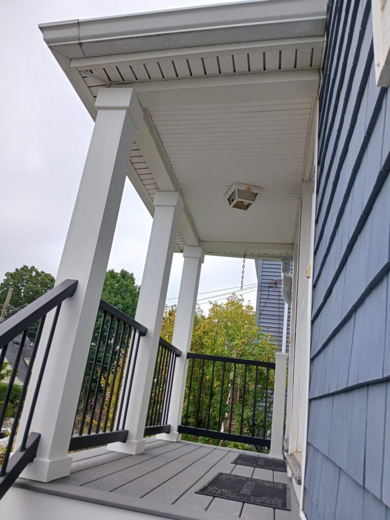 Overhead view of custom porch by Monroy's Carpenters Inc in Brighton MA: Gray composite decking with black railings and white columns on a blue house, enhancing outdoor living in Boston suburbs.